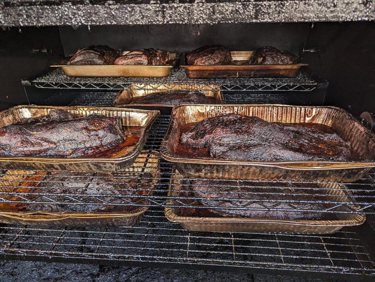Foil pans of brisket and pork racked in the smoker