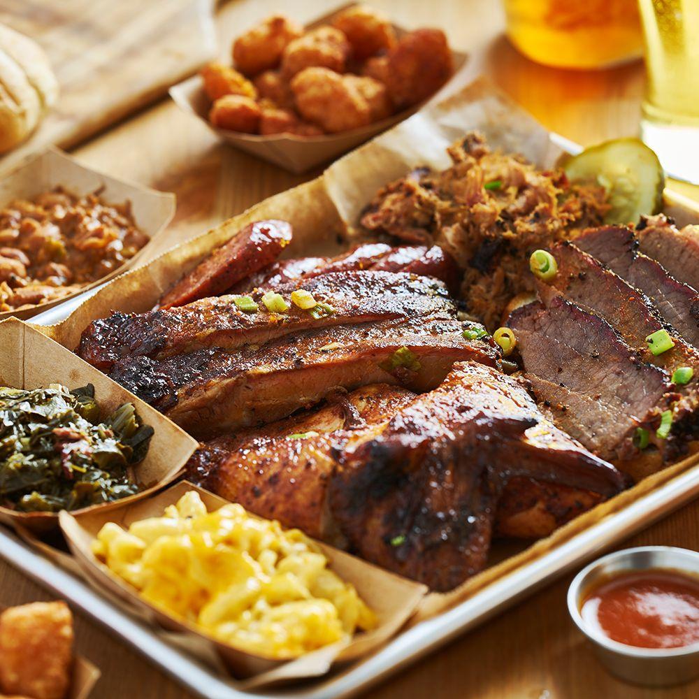A tray of ribs, sliced brisket, pulled pork, smoked chicken, mac and cheese, beans and collards